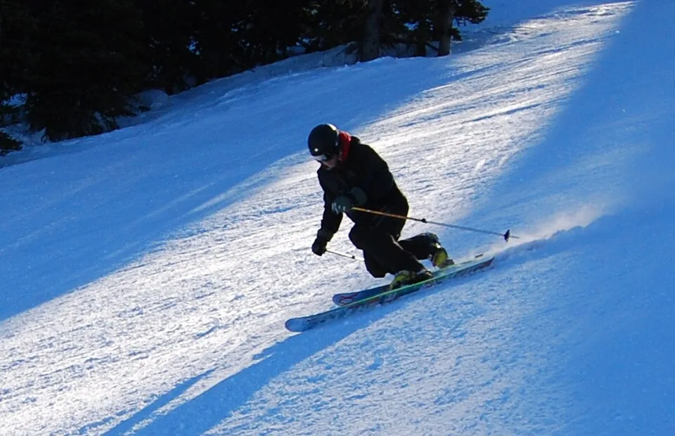 A telemark skier descending a sunlit snowy slope at Apex, British Columbia.