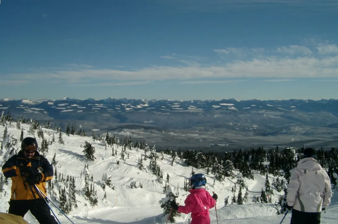 Looking out towards the Monashee mountains at the top of the Powder Chair, Big White Ski Resort. People in fore ground are skiers who have just disembarked from the lift. Chairlift in distance is Ridge Rocket Express.