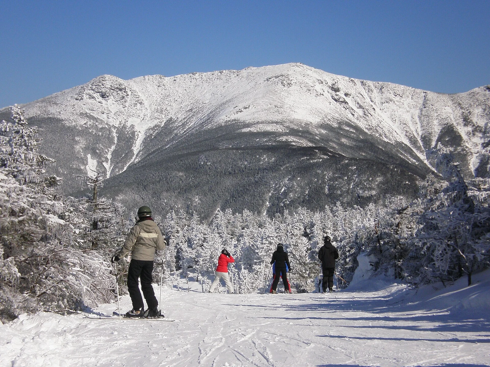 Skiers on Vista Way at Cannon Mountain, facing snowy Mount Lafayette in New Hampshire.