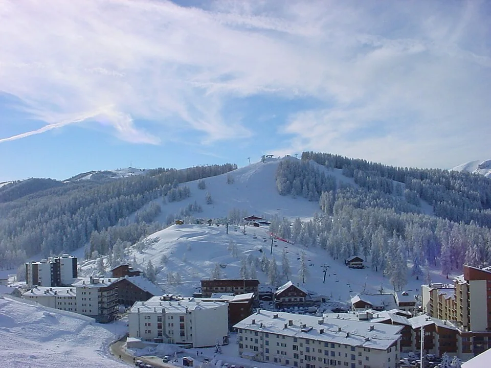 Snow-covered Valberg buildings below wooded slopes and ski runs.
