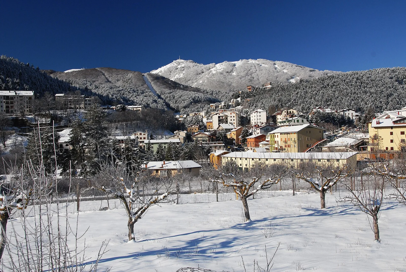 Snow-covered ground and houses in Roccaraso with mountains behind.